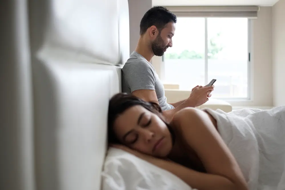 man texting while partner is asleep next to him