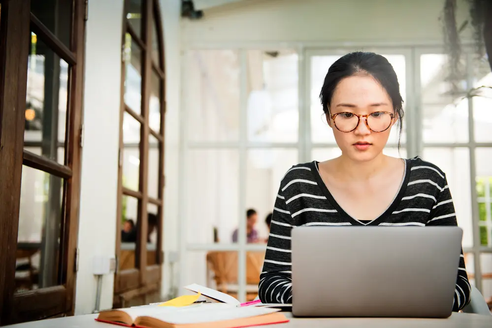 asian woman on laptop with book on table