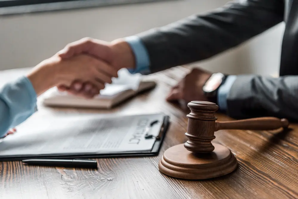 people shaking hands with a document and a gavel on the table
