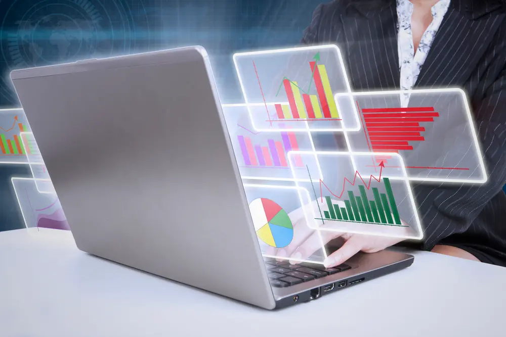 person on a laptop with graphics of charts projecting out of the laptop
